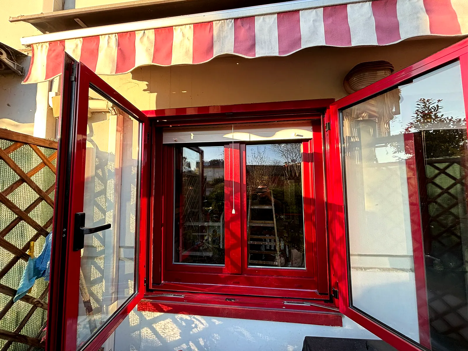 Finestra rossa a due ante aperte sotto una tenda da sole